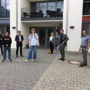 Minister Lucha und sechs weitere Personen stehen vor einem Gebäude und blicken in die Kamera