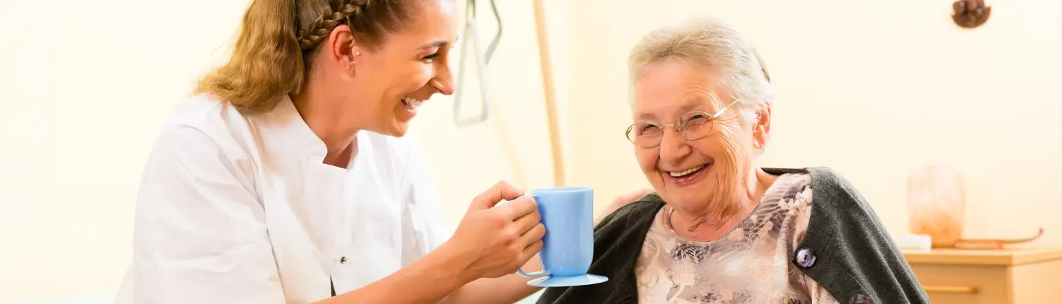 Alte Frau in Pflegeheim bekommt Getränk von Pflegepersonal